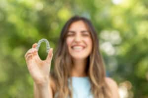 Smiling woman holding Invisalign® aligner in Houston